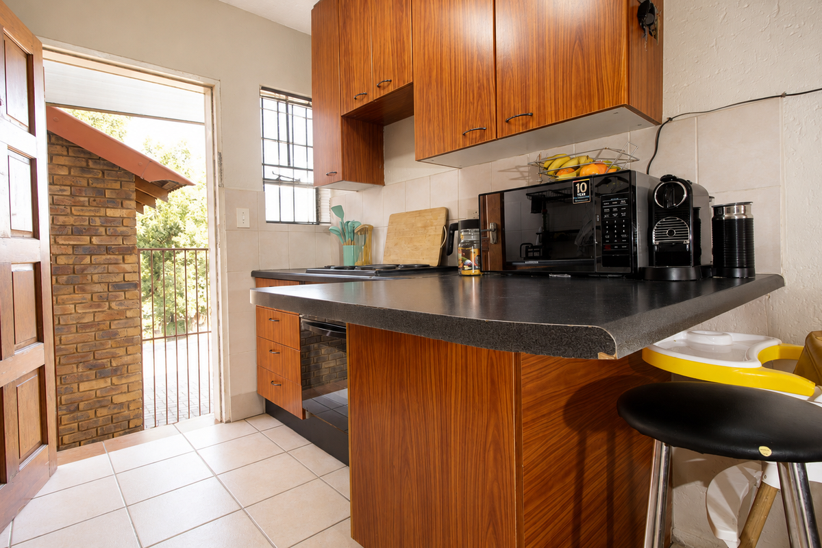 Compact kitchen featuring wood-look cabinetry, laminate countertops, built-in oven and hob, with direct access to an outdoor area.