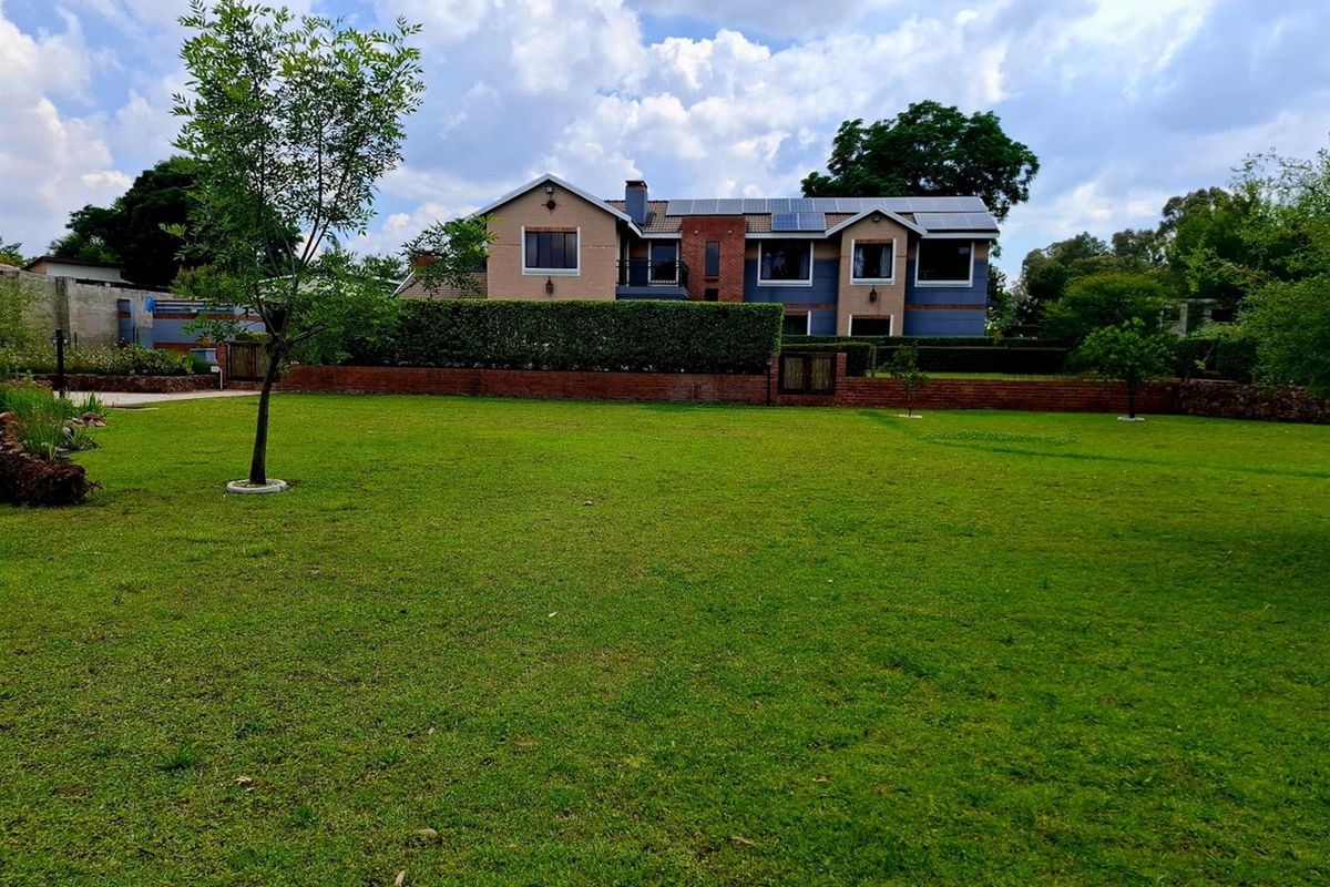 A spacious rear garden view featuring a well-maintained lawn, mature hedging, and a multi-story residential building equipped with solar panels.