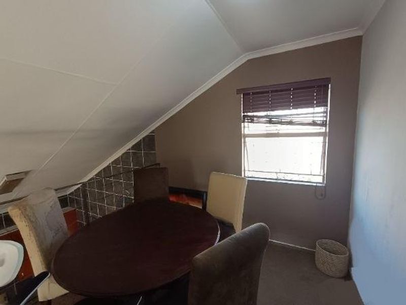 Dining area featuring a sloped ceiling, tiled wall accent, and window with venetian blinds, requiring cosmetic updates to improve the overall aesthetic.