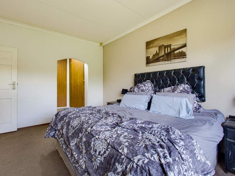 A spacious bedroom featuring neutral walls, carpeted flooring, and a distinct arched doorway leading to built-in storage cupboards.