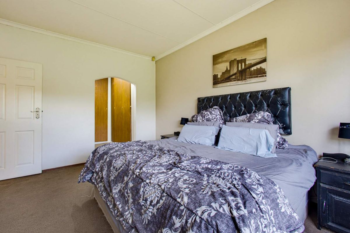 A spacious bedroom featuring neutral walls, carpeted flooring, and a distinct arched doorway leading to built-in storage cupboards.