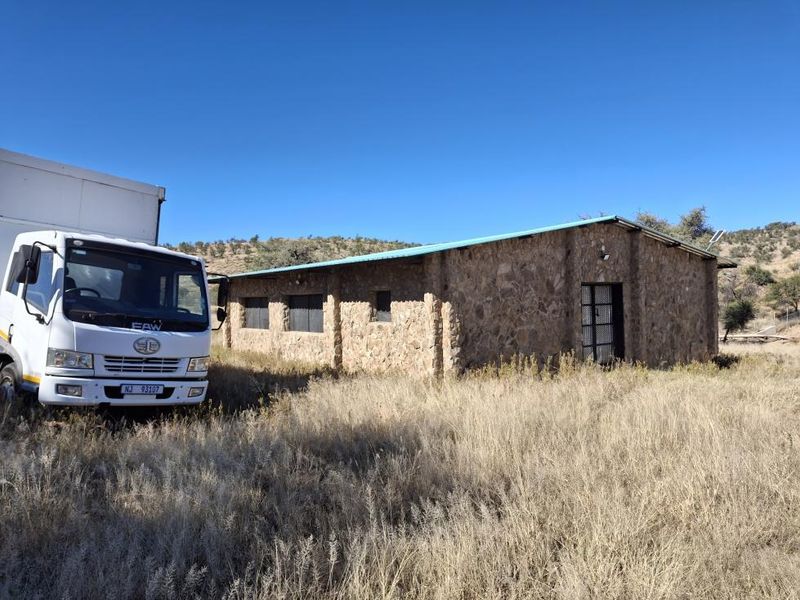 A rustic stone-clad outbuilding or structure situated on a rural small holding, featuring a metal roof and security gate access.