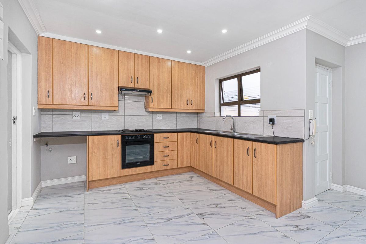 Modern kitchen featuring light wood cabinetry, dark countertops, built-in oven, extractor fan, and marble-look tiled flooring.