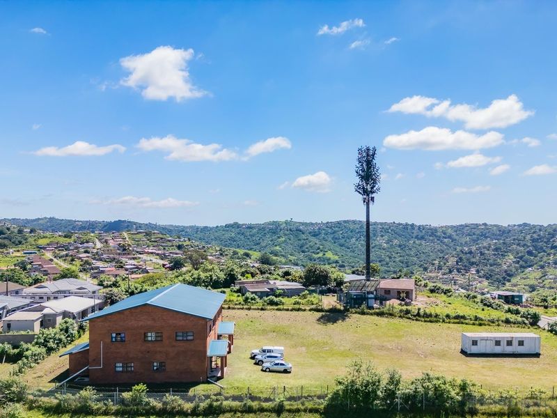 Aerial view of a residential property featuring a brick building, open land, and a telecommunications tower set against a hilly landscape.