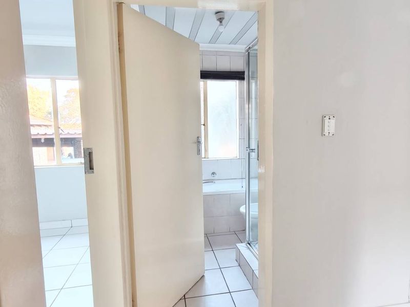 A view from a hallway looking into a bathroom featuring a shower enclosure and bathtub, with tiled flooring throughout.