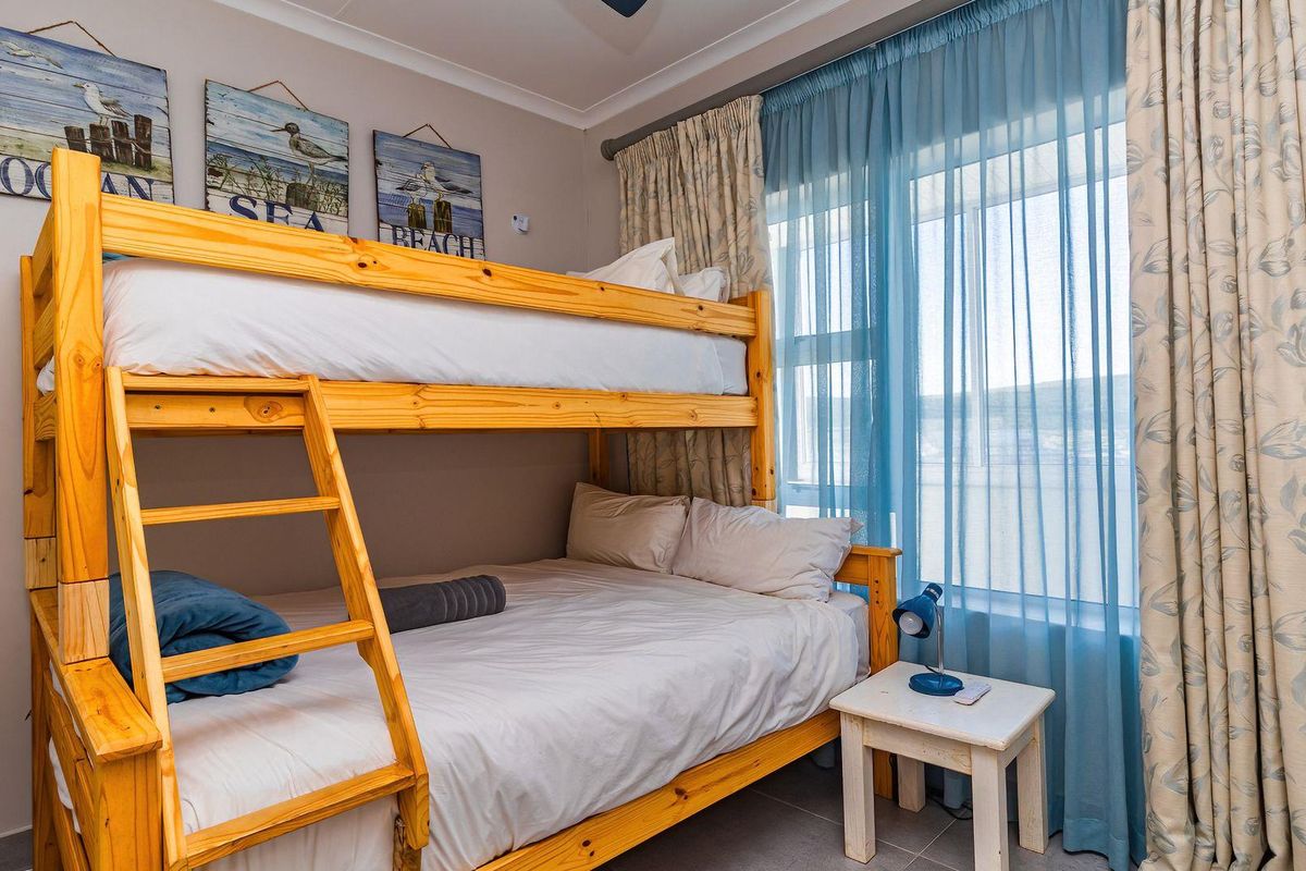 A compact bedroom featuring tiled flooring, a ceiling fan, and large windows with layered curtains, providing natural light and functional space.