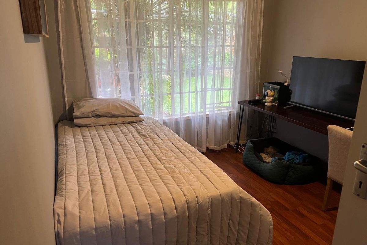 A functional bedroom featuring laminate flooring and a large window that allows for natural light and garden views.