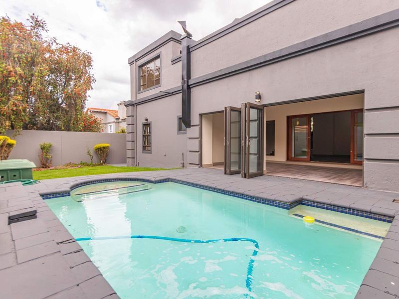 Rear exterior view featuring a swimming pool with paved surround, bi-fold doors leading to the interior, and a private garden area.