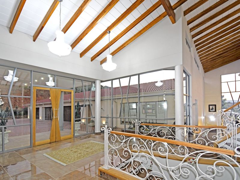 Spacious double-volume entrance hall featuring vaulted ceilings with exposed timber beams, large glass panels, and an elegant wrought iron staircase.