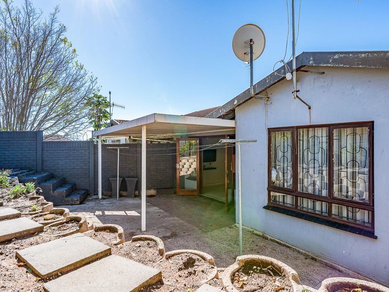 Rear exterior view of the townhouse featuring a covered patio area, paved garden sections, and brick boundary walls.