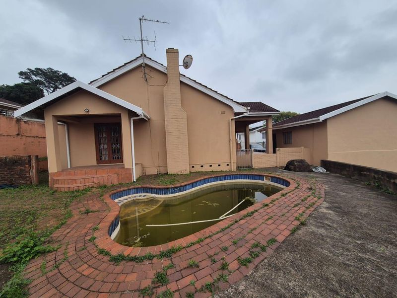 Rear exterior view of the townhouse featuring a swimming pool, covered patio area, and paved surroundings in need of maintenance.