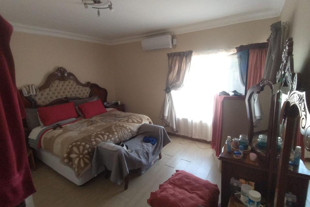 A spacious bedroom featuring laminate flooring, coving, and a wall-mounted split-system air conditioner unit.