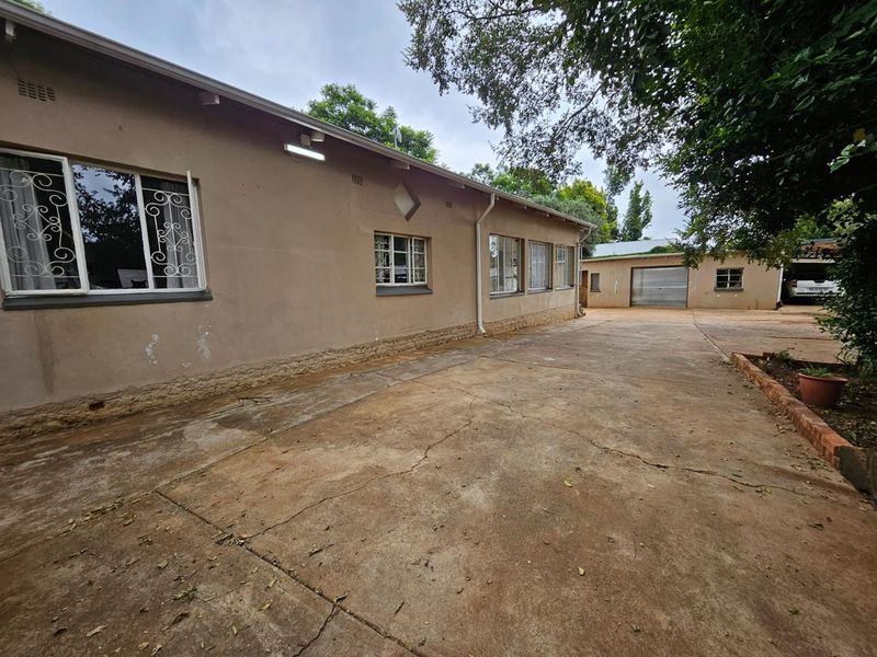 Rear exterior view of the property featuring a large concrete driveway, security bars on windows, and a detached garage structure.