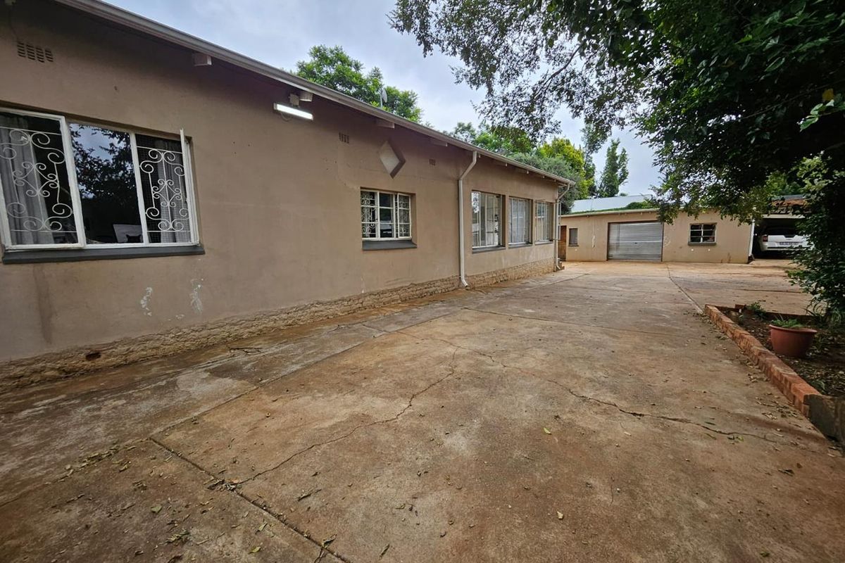 Rear exterior view of the property featuring a large concrete driveway, security bars on windows, and a detached garage structure.