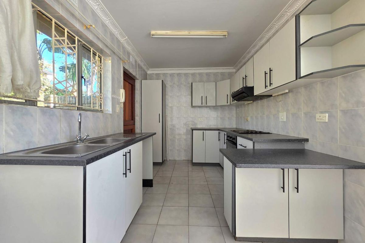 A functional kitchen featuring tiled walls, laminate countertops, built-in cabinetry, and a double basin sink with a window view.