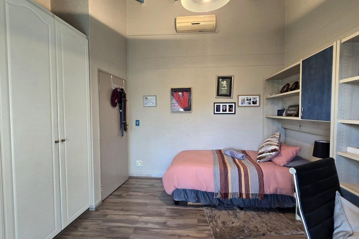 A bedroom featuring built-in cupboards, integrated shelving, wood-look flooring, and a wall-mounted air conditioning unit.
