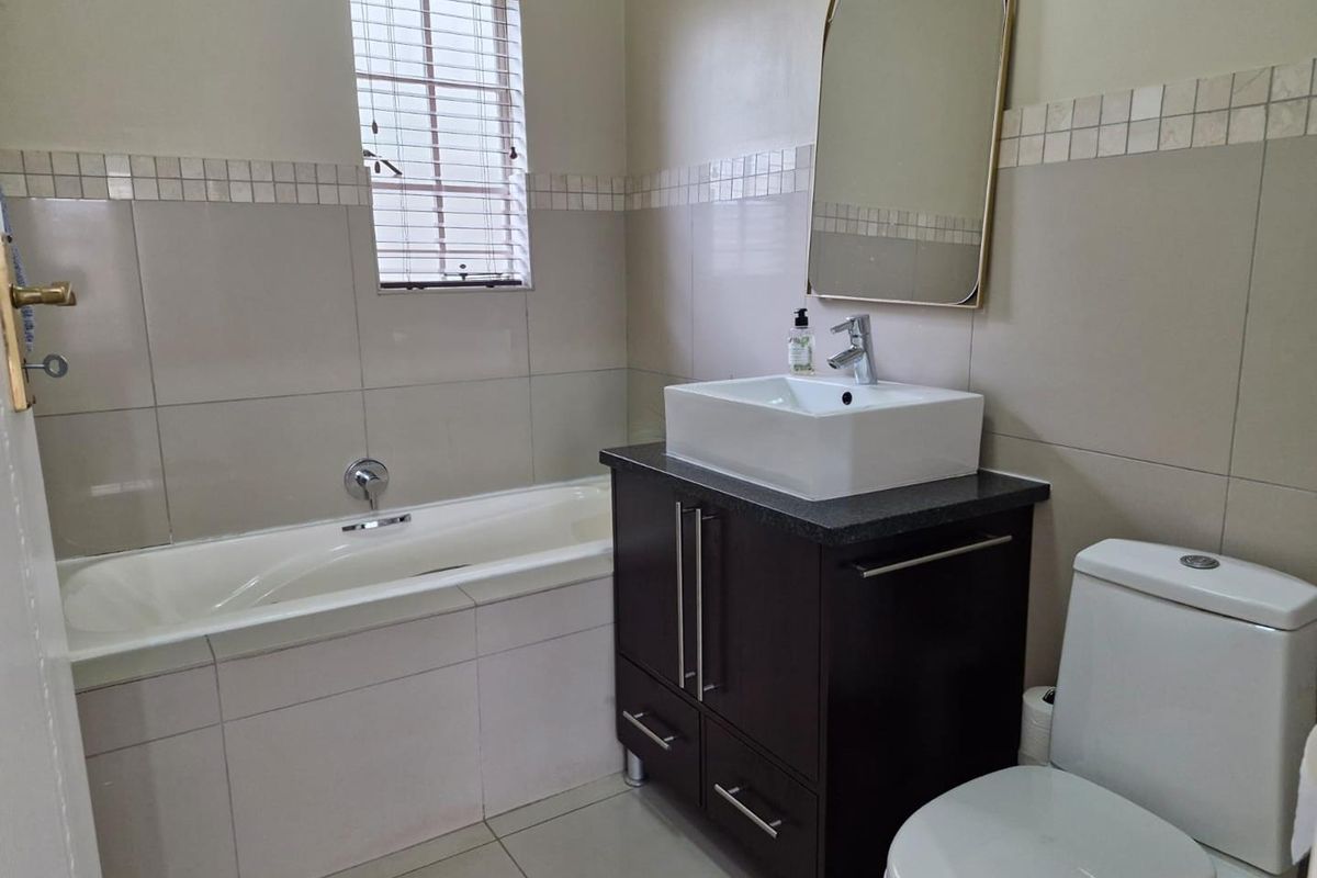 A clean, functional bathroom featuring a built-in vanity with a vessel sink, a bathtub, and neutral wall tiling.
