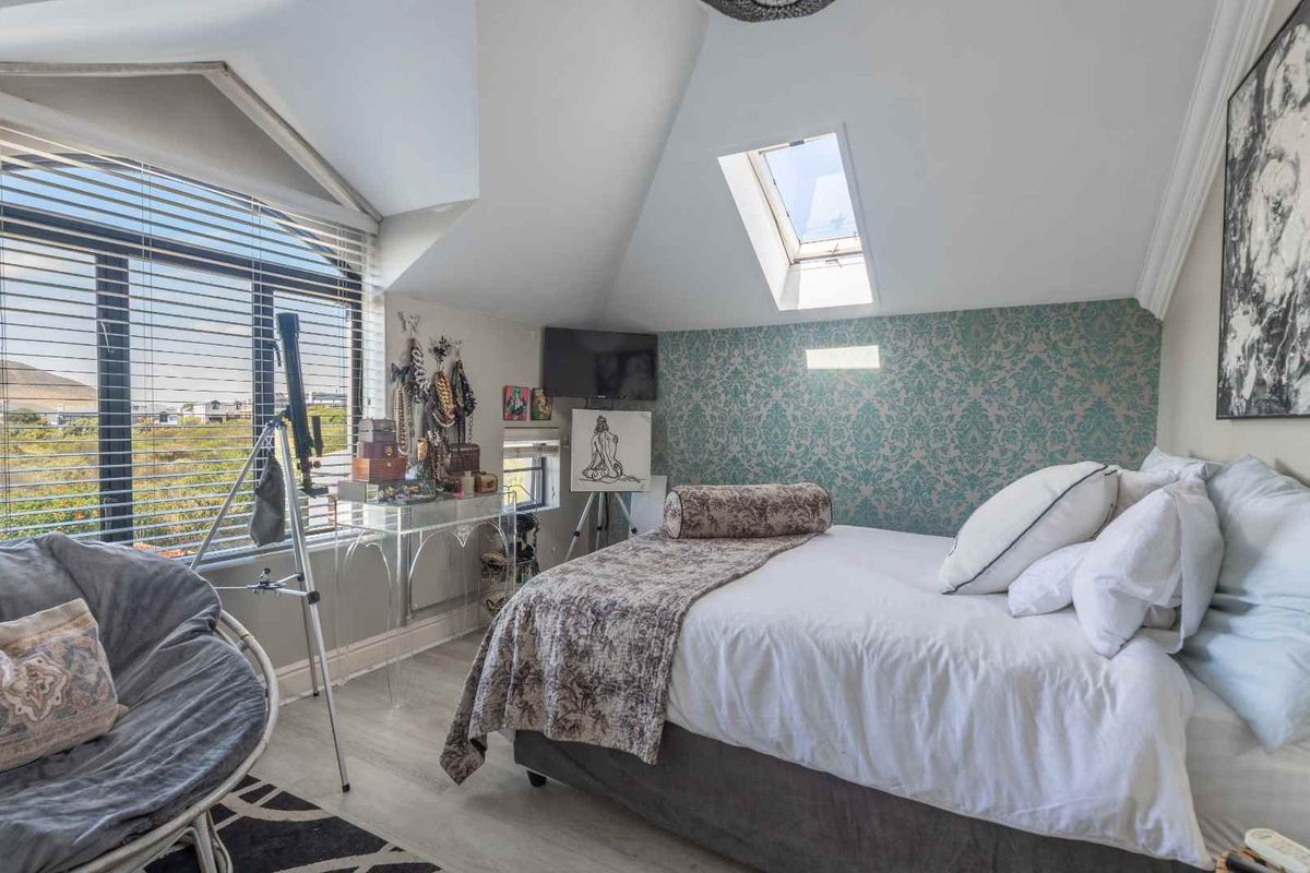 A bright bedroom featuring a vaulted ceiling, a skylight, and a feature wall with patterned wallpaper, offering natural light and a view.