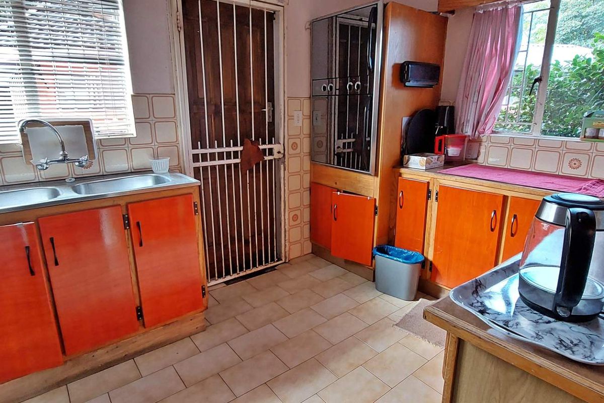 A functional kitchen featuring dated orange cabinetry, tiled splashbacks, double stainless steel sink, and a security gate leading to the exterior.