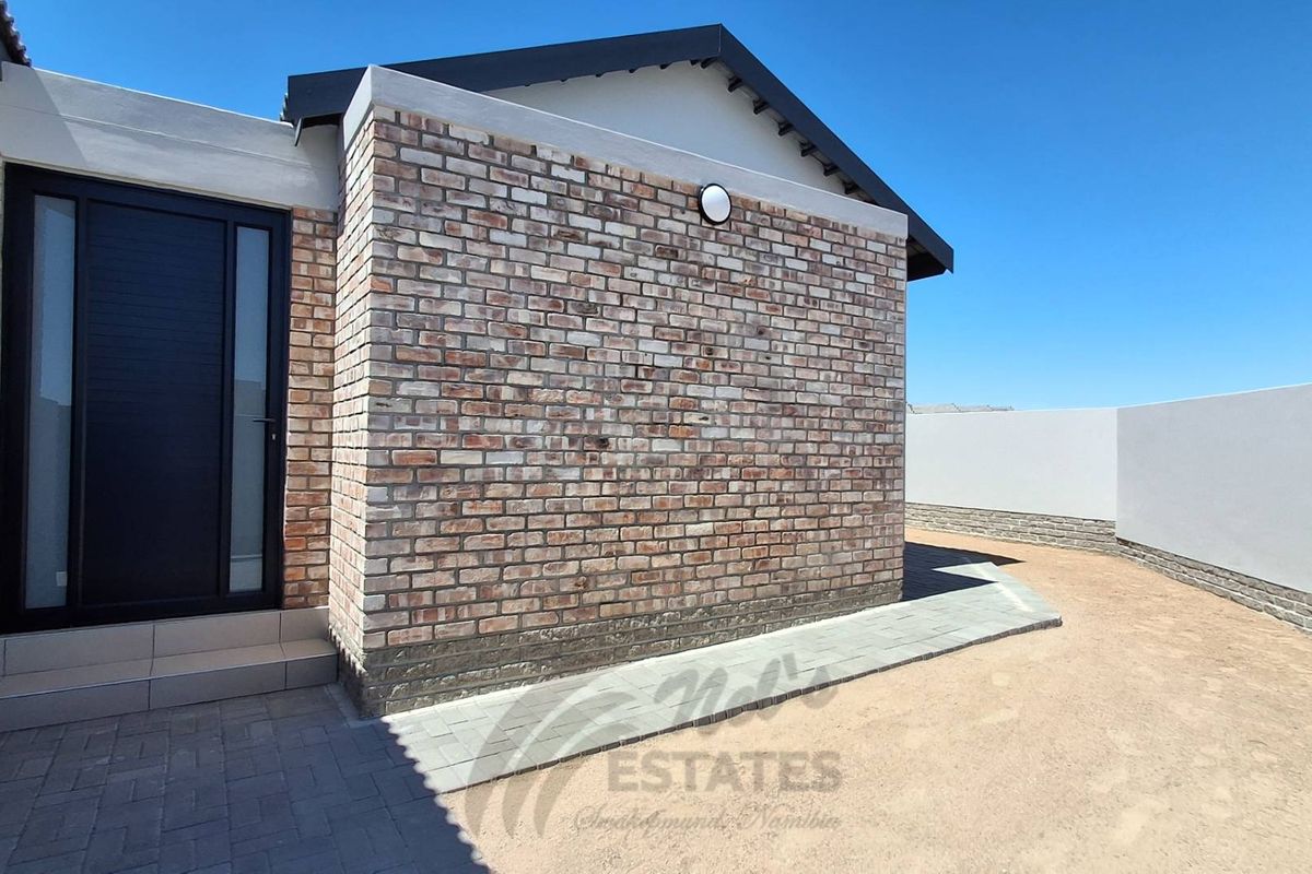 Exterior view of the property featuring a modern brick facade, paved walkway, and a secure entrance door.