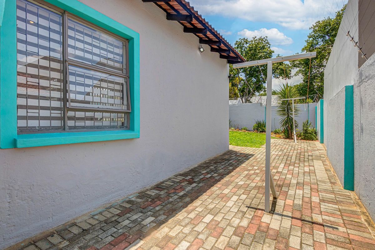 A paved rear exterior area featuring a metal washing line, perimeter wall with security fencing, and a small garden section.