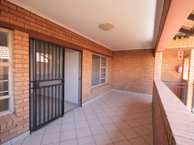 A spacious covered balcony featuring exposed brick walls, tiled flooring, and a secure sliding door entrance.