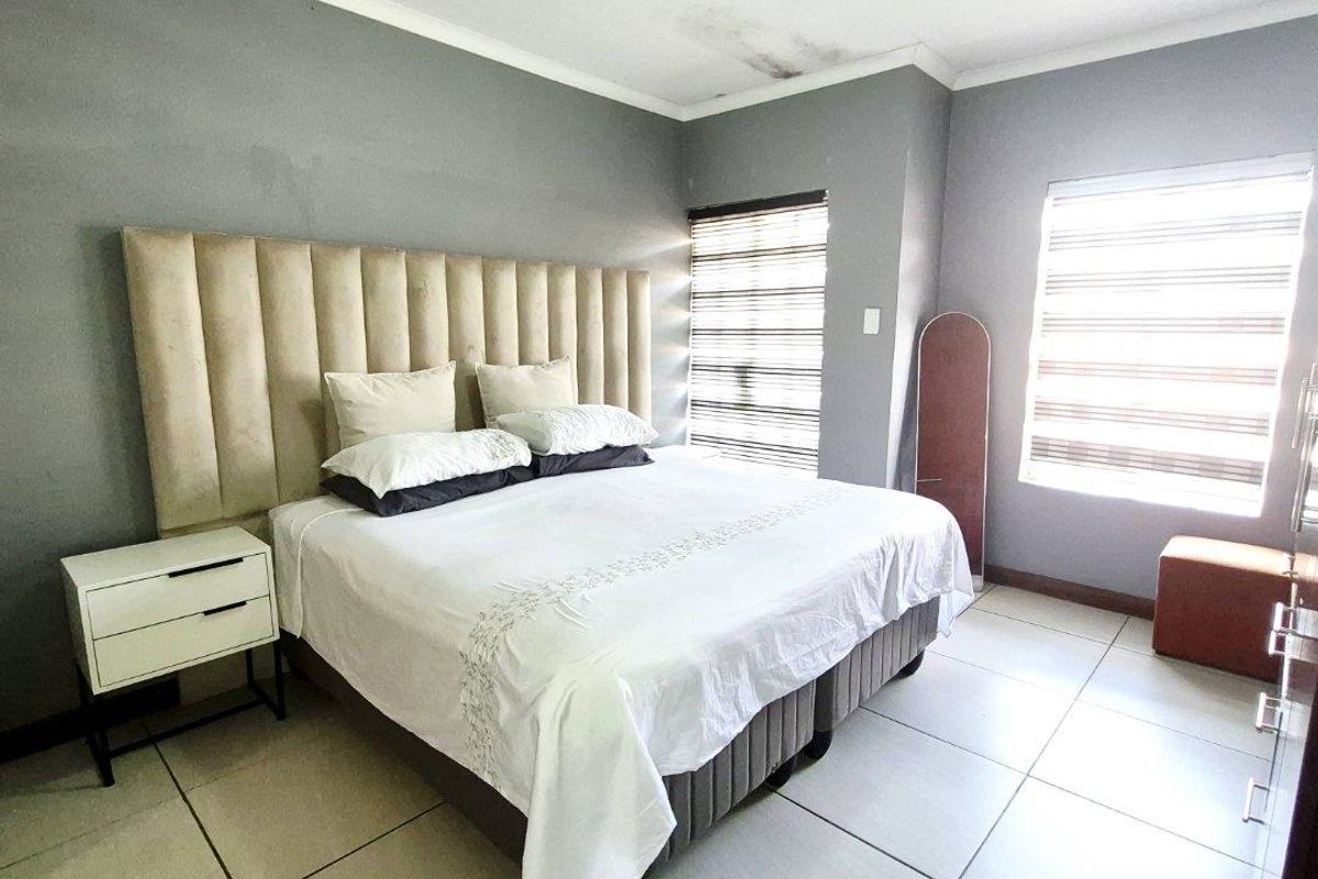 A bedroom featuring tiled flooring, dual windows with fitted blinds, and a neutral grey wall finish.