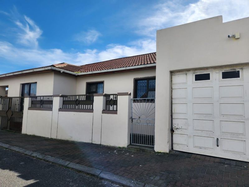 Front exterior view of a single-story house featuring a tiled roof, boundary wall with security gate, and a single garage.