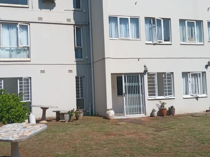 Rear elevation of a multi-story apartment building featuring ground floor access with security gates and windows overlooking a communal garden area.