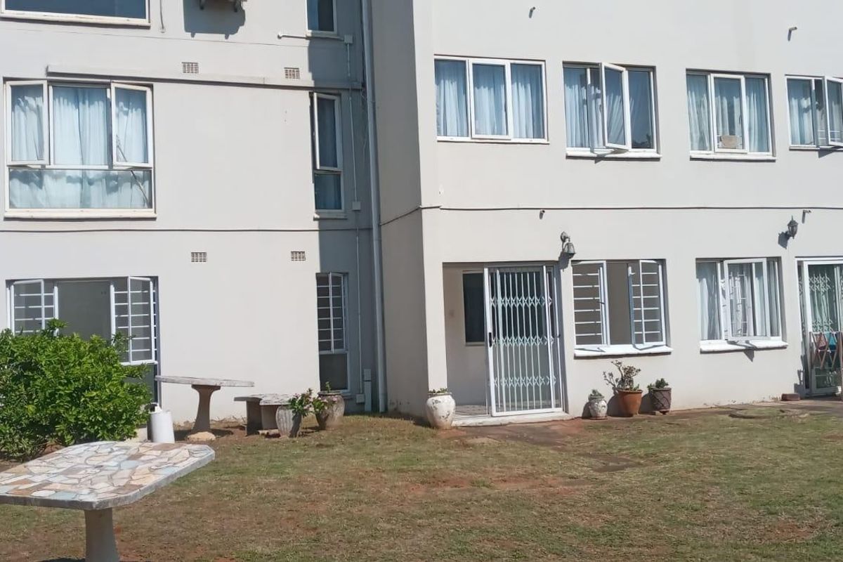 Rear elevation of a multi-story apartment building featuring ground floor access with security gates and windows overlooking a communal garden area.