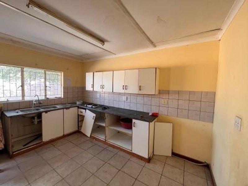 A dated kitchen featuring built-in cabinetry, tiled backsplash, and tiled flooring. The space requires renovation and repairs to the cabinetry and wall finishes.