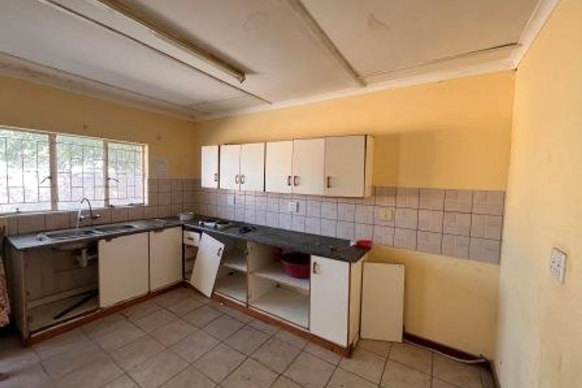 A dated kitchen featuring built-in cabinetry, tiled backsplash, and tiled flooring. The space requires renovation and repairs to the cabinetry and wall finishes.