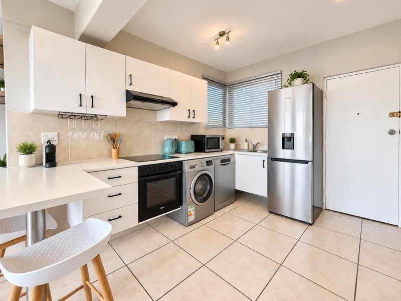 Modern kitchen featuring white cabinetry, tiled flooring, integrated oven and hob, and a stainless steel sink with convenient under-counter appliance space.