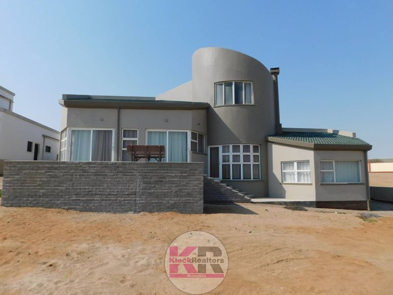 Rear view of a modern house featuring a distinctive curved architectural design, raised stone patio, and multiple sliding glass doors.