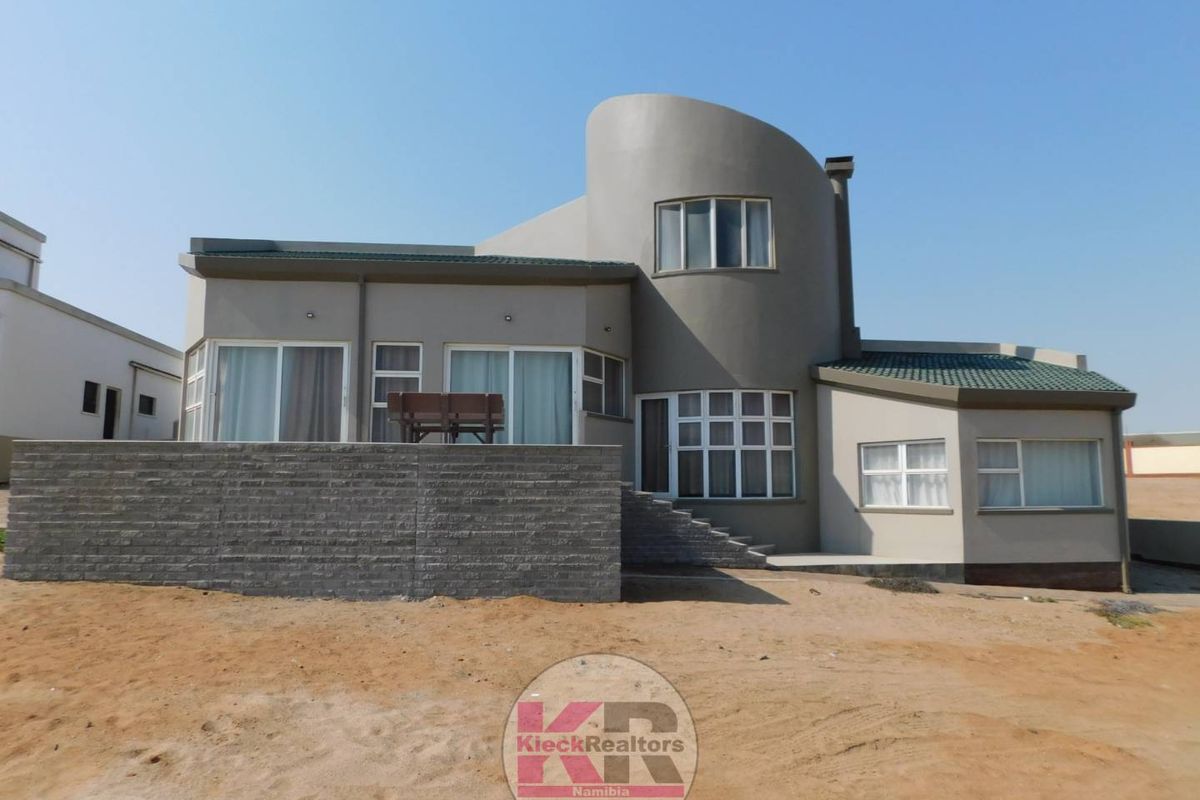 Rear view of a modern house featuring a distinctive curved architectural design, raised stone patio, and multiple sliding glass doors.