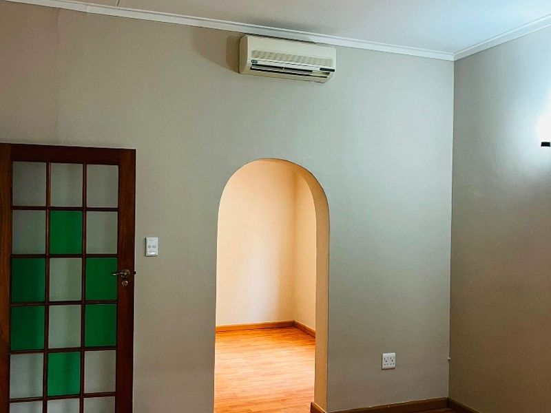 An empty living area featuring polished timber flooring, an arched transition to an adjacent room, and a wall-mounted air conditioning unit.