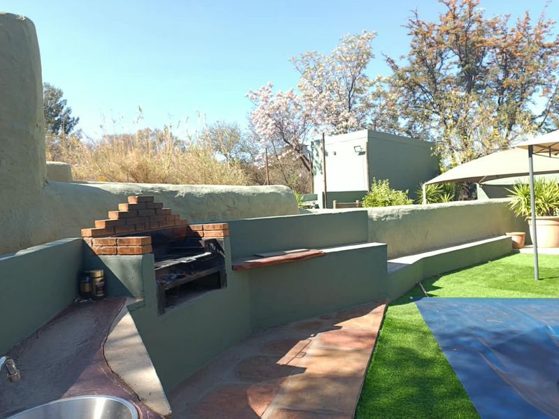 Outdoor entertainment area featuring a built-in brick braai, integrated seating wall, sink, and stone paving adjacent to a pool area.