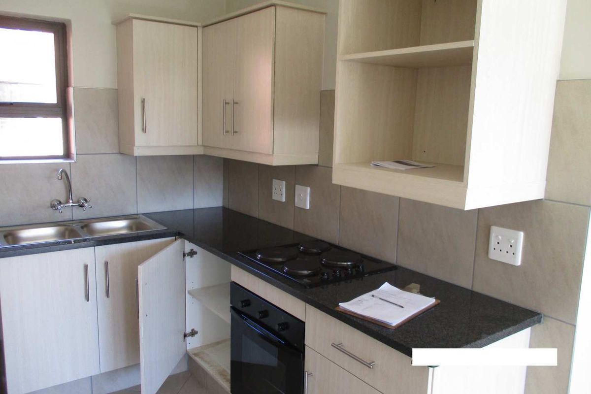 A functional kitchen featuring light wood-finish cabinetry, dark granite countertops, a built-in oven, and a four-plate electric hob with tiled splashbacks.