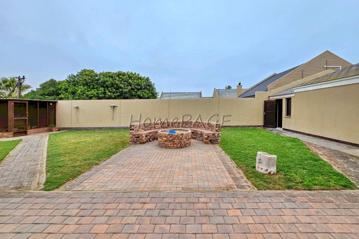 A private rear garden featuring a paved patio area, a built-in brick fire pit with seating, and a perimeter boundary wall.