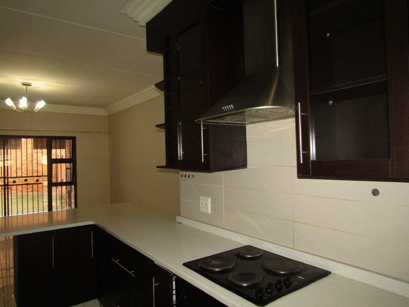 A functional kitchen featuring dark wood cabinetry, stone countertops, an electric hob, and a stainless steel extractor fan, with an adjacent security gate.