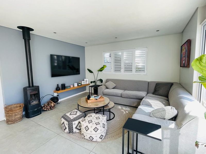 A bright and modern living room featuring a sleek freestanding fireplace, tiled flooring, and plantation shutters, creating a comfortable and inviting atmosphere.