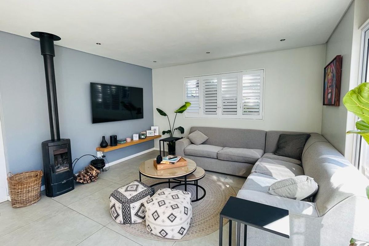 A bright and modern living room featuring a sleek freestanding fireplace, tiled flooring, and plantation shutters, creating a comfortable and inviting atmosphere.