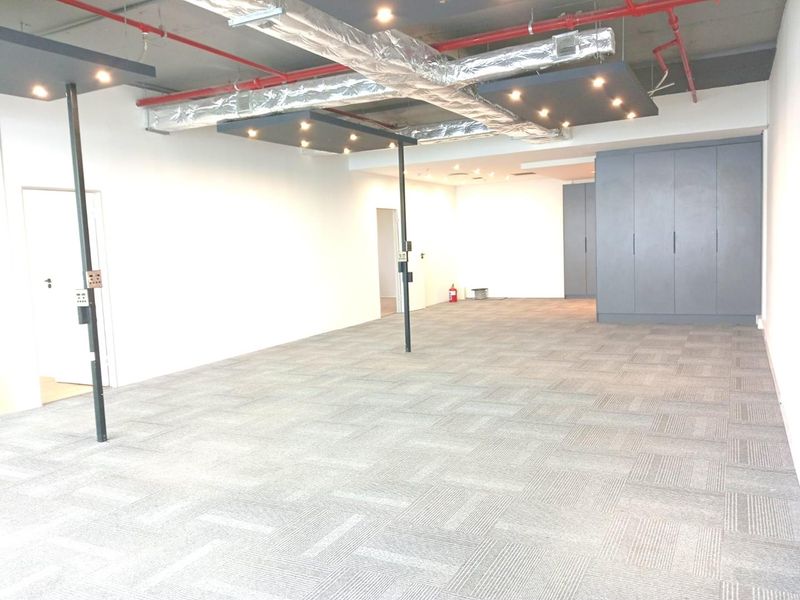 Spacious open-plan office area featuring exposed industrial ceilings, carpet tile flooring, recessed lighting, and integrated storage cabinetry.