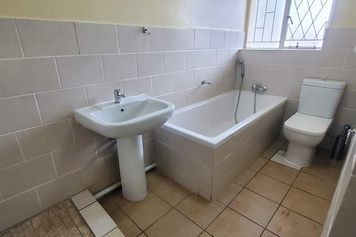 A functional bathroom featuring a pedestal basin, a built-in bathtub with a handheld shower attachment, and a standard toilet.