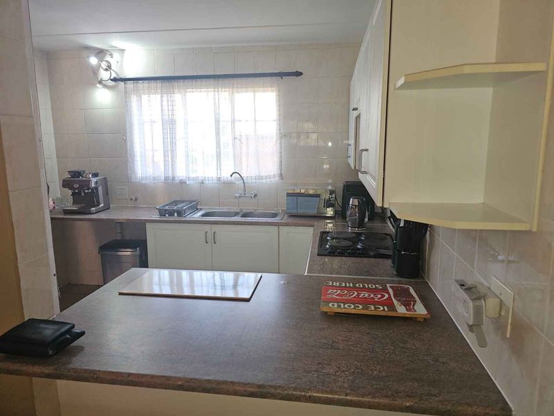 A functional kitchen featuring built-in cabinetry, a double basin sink, electric hob, and tiled backsplash with ample counter space.