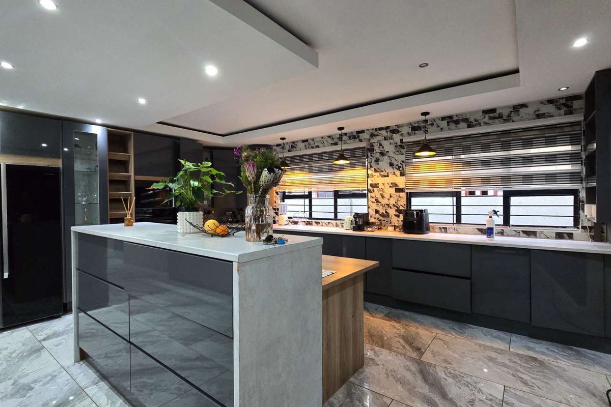 Modern kitchen featuring high-gloss cabinetry, a central island with stone countertops, integrated appliances, and stylish tiled flooring with recessed and pendant lighting.
