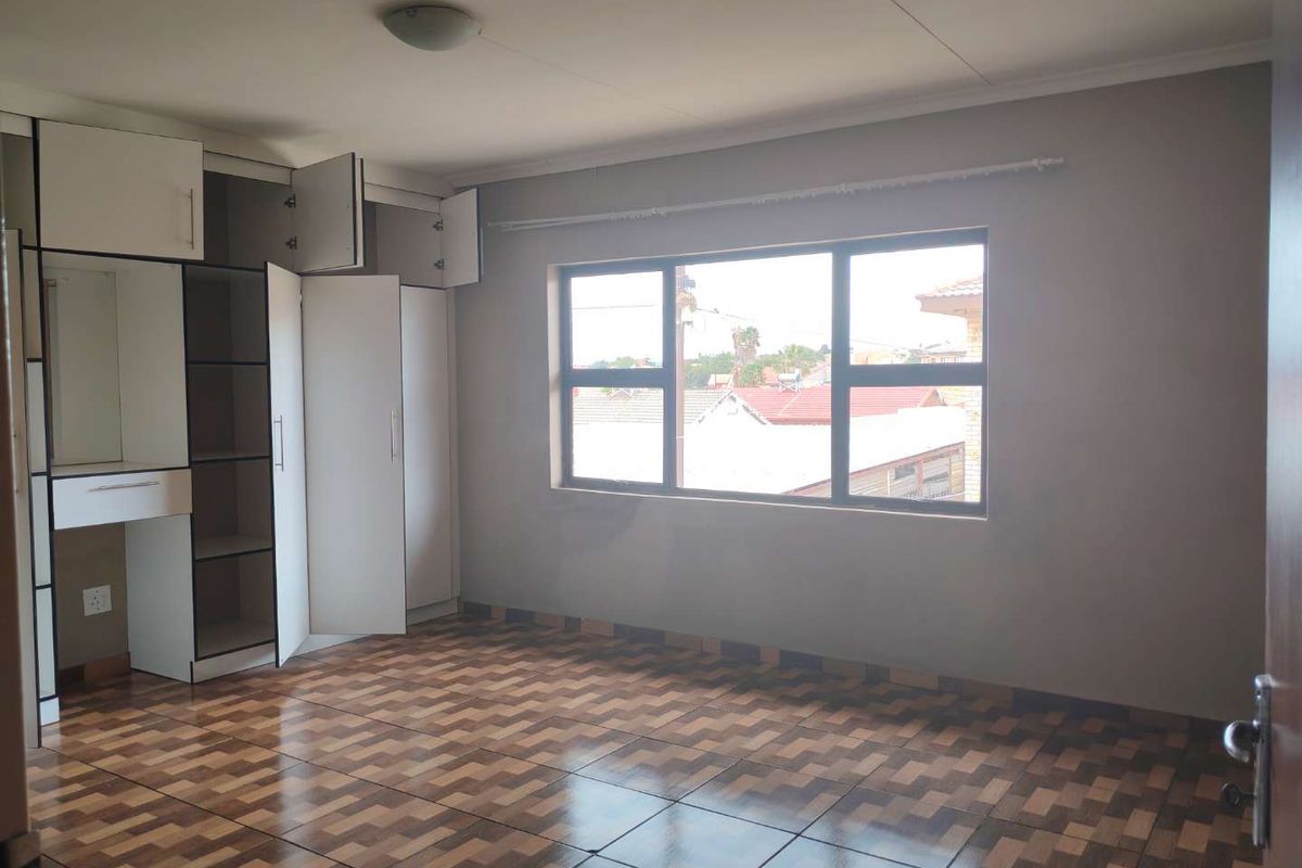 A spacious bedroom featuring built-in cupboards, tiled flooring, and large windows that provide natural light.