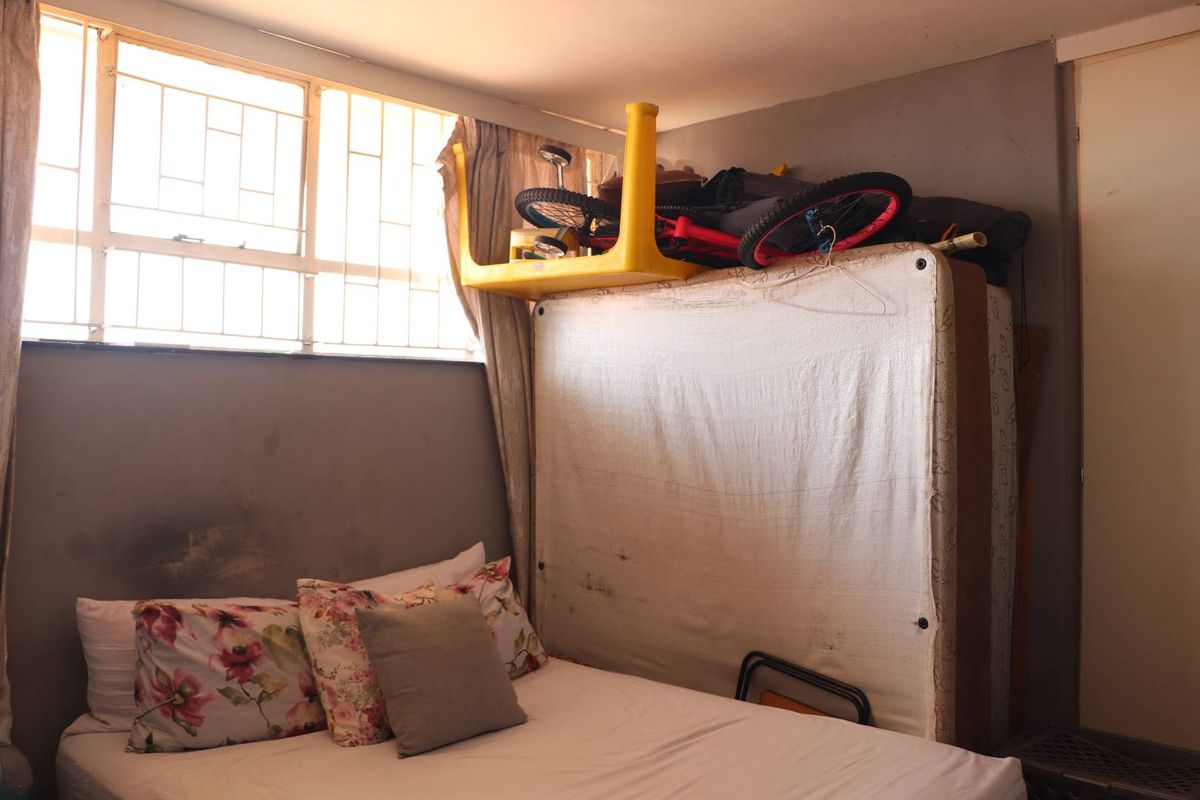 A bedroom featuring a large window with security bars, providing natural light. The space requires cosmetic updates to the wall finishes.