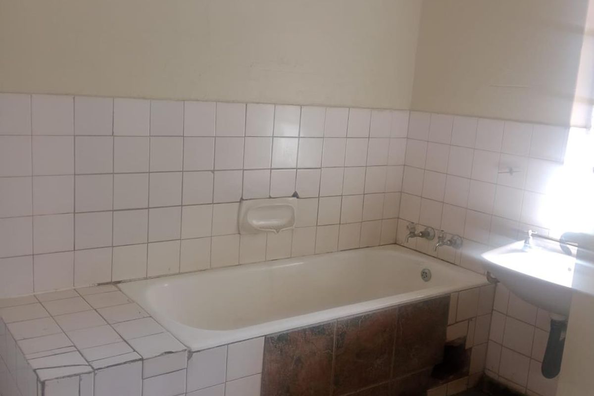 A dated bathroom featuring a built-in bathtub with tiled surround and a wall-mounted basin, requiring cosmetic updates and repairs to the tiling.