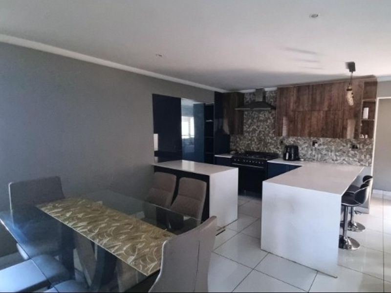 Open-plan kitchen and dining area featuring modern cabinetry, stone countertops, a central island, and tiled flooring throughout.